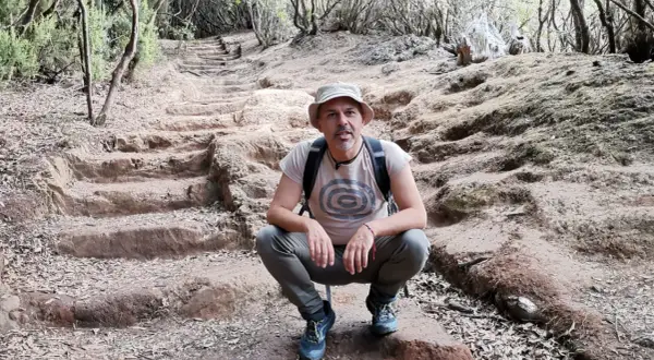 Hombre con sombrero y mochila en el sendero de los sentidos Tenerife, rodeado de vegetación y escalones de tierra.