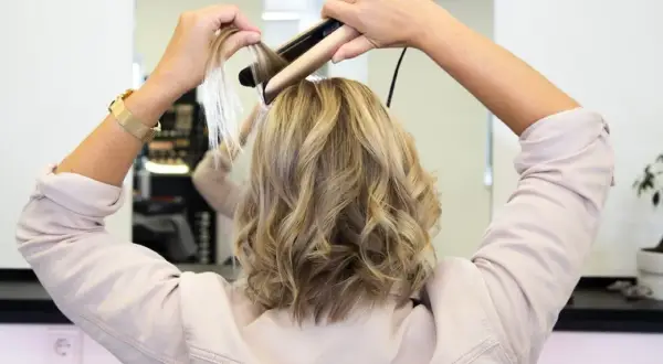Frau stylt ihre Haare mit einem Glätteisen, um sanfte Wellen zu kreieren.