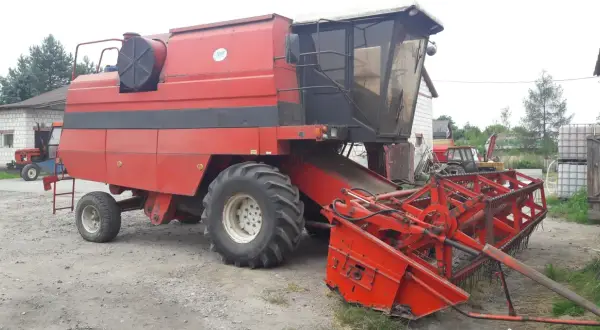 Czerwona maszyna rolnicza Bizon BS Z110 z hederem, gotowa do pracy na polu.