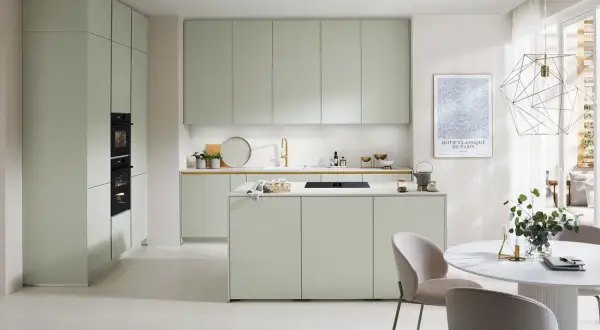 Moderna cocina verde con isla central, electrodomésticos integrados y una mesa redonda con sillas.
