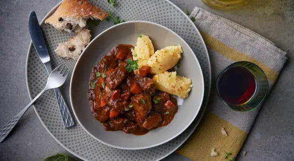 Herzhaftes Spezzatino di manzo mit cremigem Polenta, dazu ein Glas Rotwein und rustikales Brot.