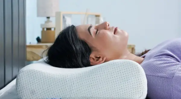 Woman sleeping on her back with head cradled by an ergonomic pillow, demonstrating the **forma correcta de dormir con almohada** for optimal neck support.