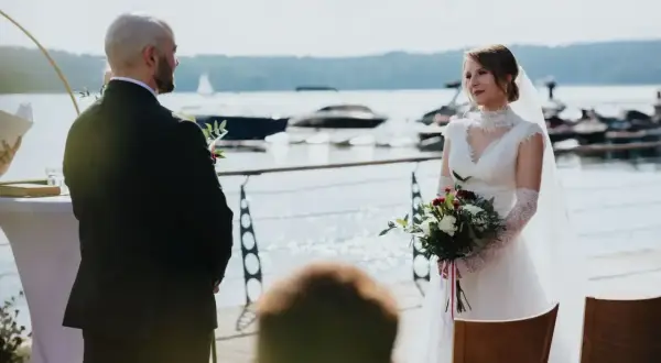 Para młoda podczas ślubu rzymskiego nad jeziorem. Panna młoda w białej sukni z bukietem, pan młody w garniturze.