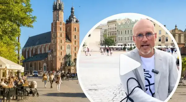 Mężczyzna w okularach opowiada o tym, czy jest krakow safe, na tle Rynku Głównego z Kościołem Mariackim.