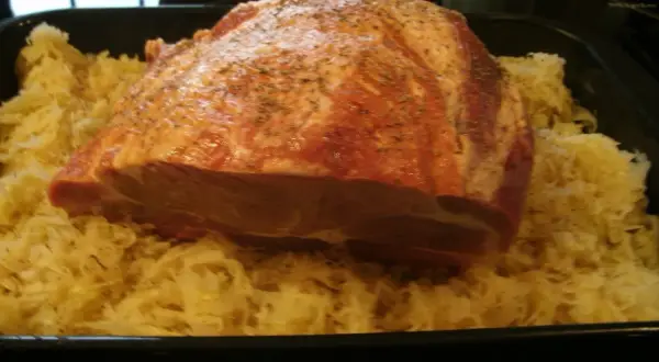 Rohes Schweinefleisch mit Gewürzen liegt auf Sauerkraut in einer Bratreine. Bereit zum Kochen.