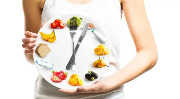 Une assiette en forme d'horloge illustrant la chrono nutrition avec des fruits, légumes, pain et eau.