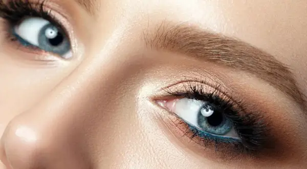 Blonde Haarfarbe betont blaue Augen. Nahaufnahme eines weiblichen Auges mit blauem Eyeliner und goldenem Lidschatten.