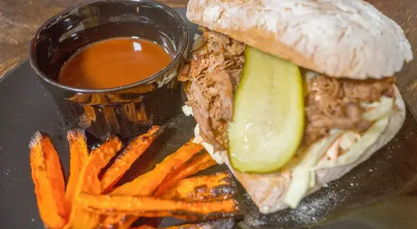 Pulled pork-macka med krispiga sötpotatispommes och en skål med smakrik sås till pulled pork.