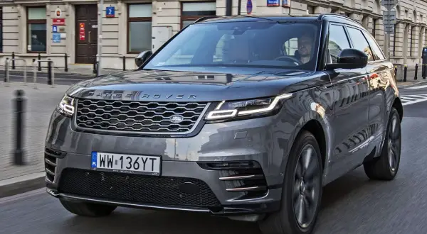 Szary Range Rover Velar jedzie ulicą w mieście. Kierowca jest widoczny za kierownicą.