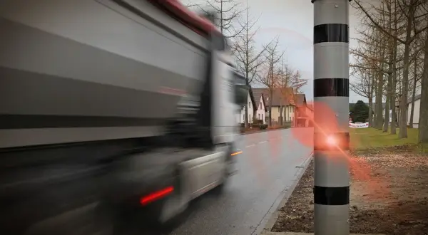 Ein Lkw rast an einem Blitzer vorbei. Der Blitz leuchtet auf, als der Fahrer zu schnell fährt.