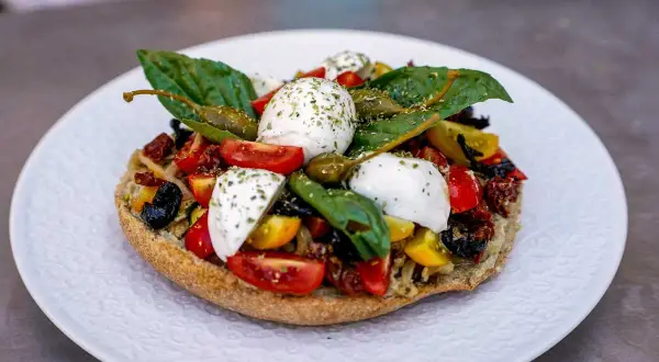 Frisches Brot belegt mit Tomaten, Kapern, Oliven und verschiedenen Mozzarella Arten, garniert mit Basilikum.