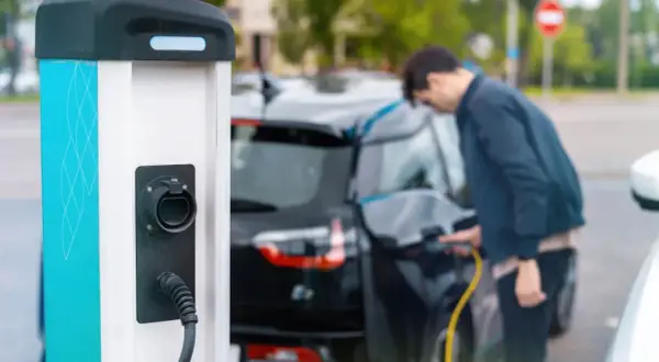 Mężczyzna ładuje czarny samochód elektryczny przy stacji ładowania.
