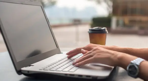 Kobieta pisze na laptopie, zastanawiając się, co zainstalować na nowym komputerze. Obok stoi kubek kawy.