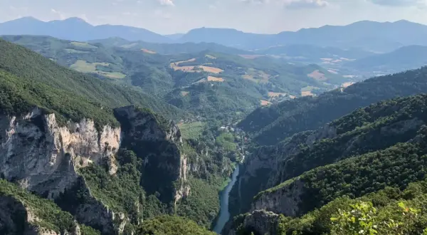 Vista mozzafiato dalla terrazza del Furlo: un fiume serpeggia tra gole rocciose e colline verdi, sotto un cielo azzurro con nuvole bianche.