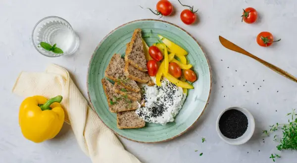 Szybkie posiłki wysokobiałkowe: twarożek z czarnuszką, pieczywo, pomidorki i papryka. Idealne na lekki lunch.