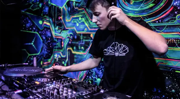 Młody DJ w słuchawkach miksuje muzykę w klubie z psychodelicznym tłem. Chcesz wiedzieć, jak zostać DJ w klubie? Zacznij od tego!