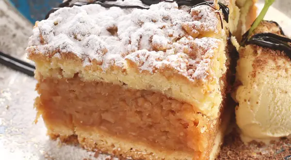 Pyszna szarlotka z kruszonką, posypana cukrem pudrem, z gałką lodów waniliowych. Idealna na deser, gdy zastanawiasz się, jak zrobić jabłka do szarlotki.