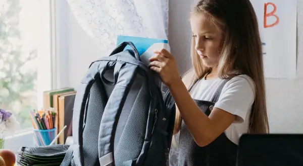 Dziewczynka wkłada książkę do plecaka. Zastanawia się, jak prać plecak w pralce, by był czysty na nowy rok szkolny.