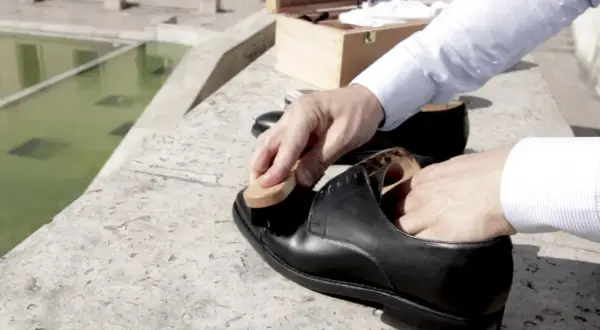 Un homme prend soin de ses chaussures noires, appliquant du cirage avec une brosse. La fréquence du cirage chaussure est essentielle pour leur longévité.