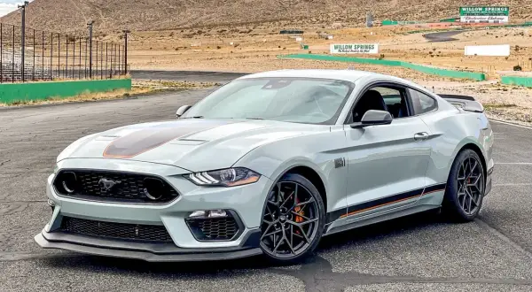 Jasnoszary Mustang GT 5.0 z pomarańczowymi akcentami na torze wyścigowym Willow Springs.