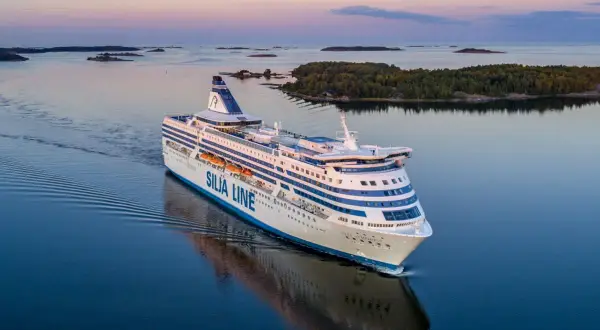 Prom Silja Line płynie przez spokojne morze, tworząc fale. W tle widać wyspy i lasy, a niebo mieni się pastelowymi barwami. Idealna podróż z Tallinna do Helsinek.