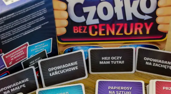 Karty z gry "Czółko Bez Cenzury" leżą na stole. Widać hasła takie jak "Opowiadanie na małpę" i "Hej! Oczy mam tutaj!".