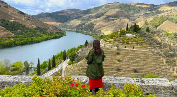 Mujer admira la impresionante **ruta del Duero**, con sus viñedos en terrazas y el río serpenteando entre colinas verdes.