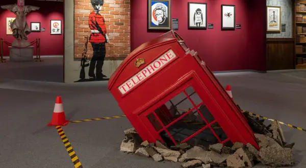 Wystawa Banksy Warszawa: przewrócona budka telefoniczna, mural z żołnierzem i prace artysty.