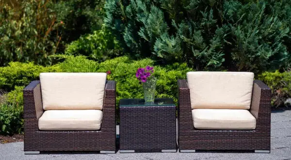 Dos sillones y una mesita de centro de ratán, perfectos para el mantenimiento de muebles de exterior. Flores moradas en un jarrón.