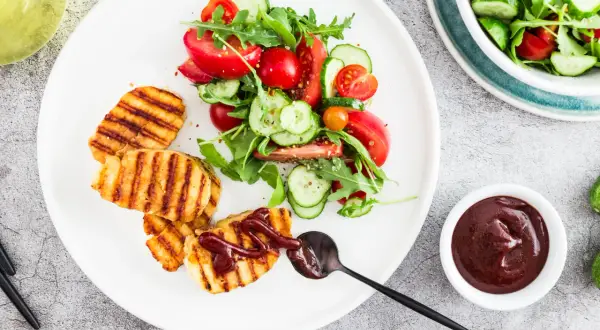 Grillowany ser halloumi z sałatką z pomidorów i ogórka, polany sosem.