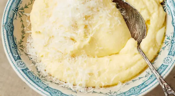 Cremige Polenta, frisch gekocht und mit Parmesan bestreut, wartet in einer blumig verzierten Schüssel auf den Löffel.