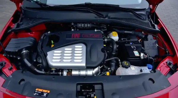 Silnik fiat bravo 1.4 t-jet w komorze pod maską. Widoczny akumulator, układ dolotowy i osłona silnika.