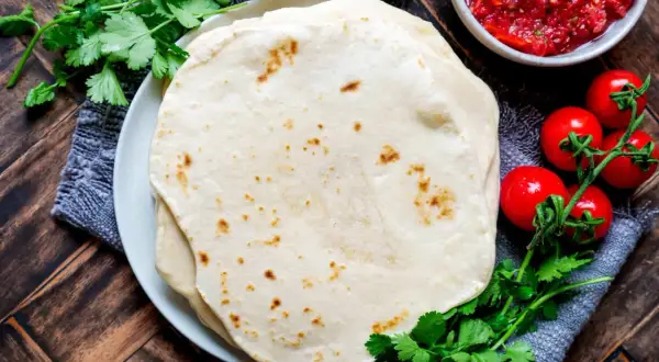 Frische Tortillas, perfekt für jedes Tortilla Rezept, mit Salsa, Tomaten und Koriander auf Holztisch.