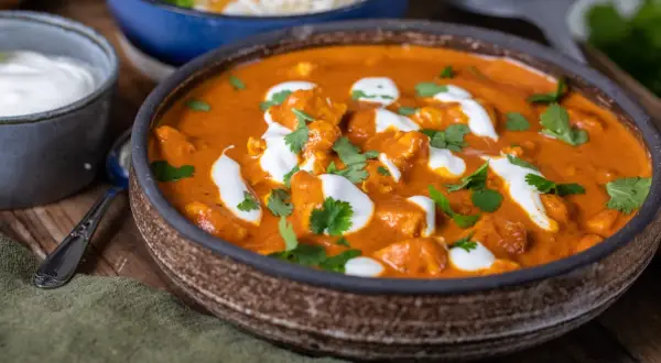 En krämig tikka masala med kycklingbitar, toppad med grädde och koriander. Serveras med ris och en skål yoghurt.