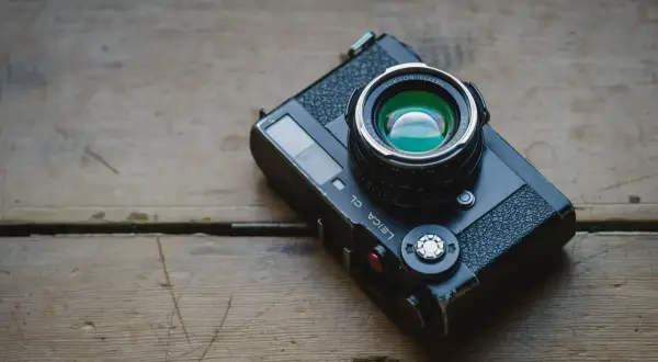 A Leica CL camera with a Nokton Classic lens rests on a weathered wooden surface, ready for a detailed review.