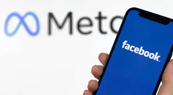 Szukasz sposobu, jak znaleźć osobę na FB po imieniu? Smartfon z logo Facebooka i symbolem Meta w tle.