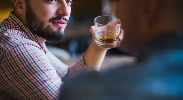 Mężczyzna z zarostem, w kratę, trzymający szklankę z bursztynowym płynem. W jego oczach widać pustkę, typową dla narcyza alkoholika.