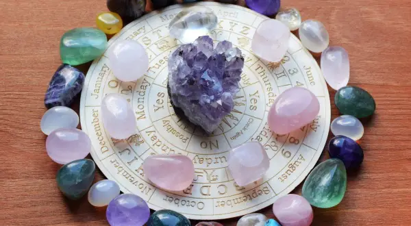 Okrąg kamieni, w tym ametyst, różowy kwarc i fluoryt, ułożony na kole zodiaku. Jaki kamień dla bliźniąt? Ametyst i cytryn mogą wspierać.