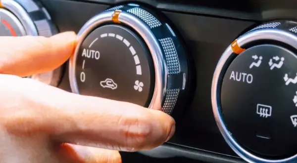 Dłoń reguluje pokrętło klimatyzacji w samochodzie, ustawiając tryb AUTO. Włączony jest czynnik chłodniczy, zapewniając komfortową temperaturę.