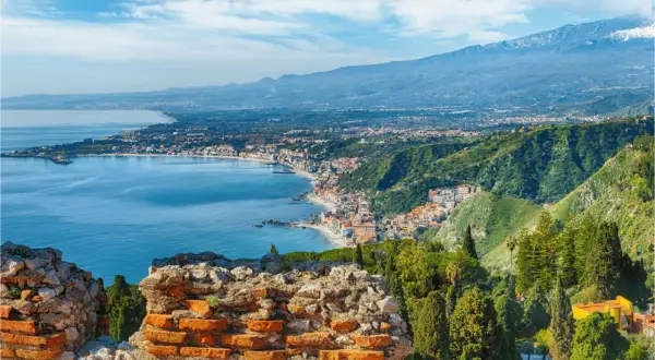 Vacker vy över kusten vid Catania, Sicilien, med det blå havet, en stad längs kusten och Etna i bakgrunden.