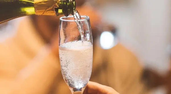 Schaumweine sorten: Ein Glas Sekt wird aus einer Flasche in ein Sektglas gegossen, das mit sprudelnden Bläschen gefüllt ist.