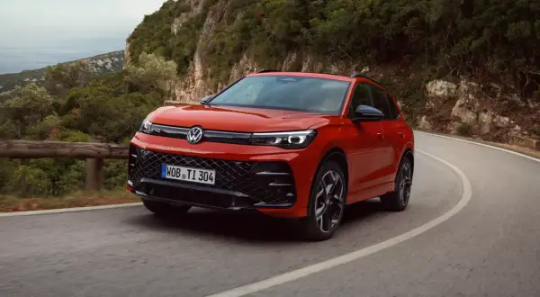 Röd Volkswagen kör på en kurvig väg i bergen. Denna hybridbil kombinerar eldrift med bensinmotor, vilket ger en flexibel körupplevelse.