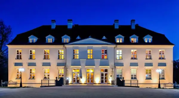 Beleuchtetes Schloss mit vielen Fenstern bei Nacht vor blauem Himmel.