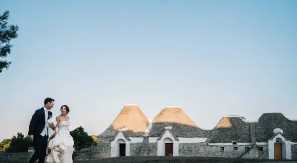 Sposi passeggiano sorridenti davanti a trulli, un'immagine perfetta per le canzoni ingresso sposi.