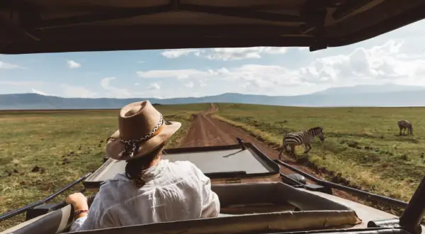 Mujer con sombrero en un safari en Tanzania, observando cebras en la sabana.