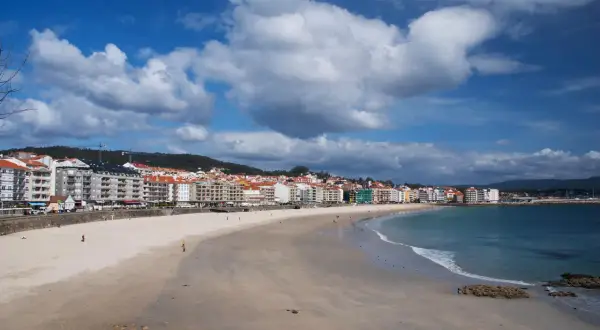 Amplia playa de Silgar con edificios residenciales al fondo y el mar azul bajo un cielo nublado.