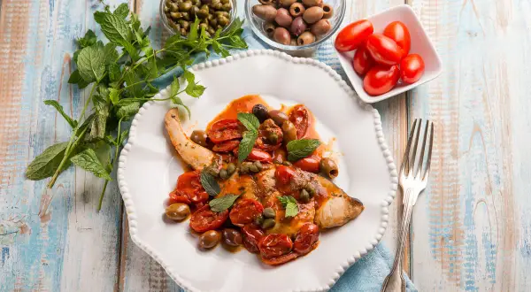 Un saporito pesce spada alla siciliana, condito con pomodorini, olive, capperi e menta fresca, pronto per essere gustato.