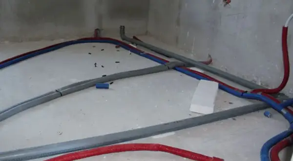 Na betonowej posadzce widać instalację wodną z czerwonych i niebieskich rur, które tworzą skomplikowany trojnik.