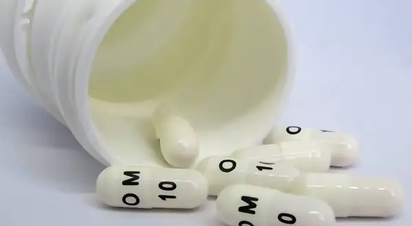Białe kapsułki z oznaczeniem "OM 10" rozsypane obok otwartego pojemnika, mogą być stosowane w leczeniu raka.