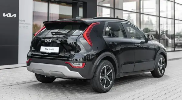 Czarny Kia Niro Hybrid stoi przed salonem. Elegancki tył auta z charakterystycznymi światłami i napisem "Niro Hybrid" przyciąga wzrok.